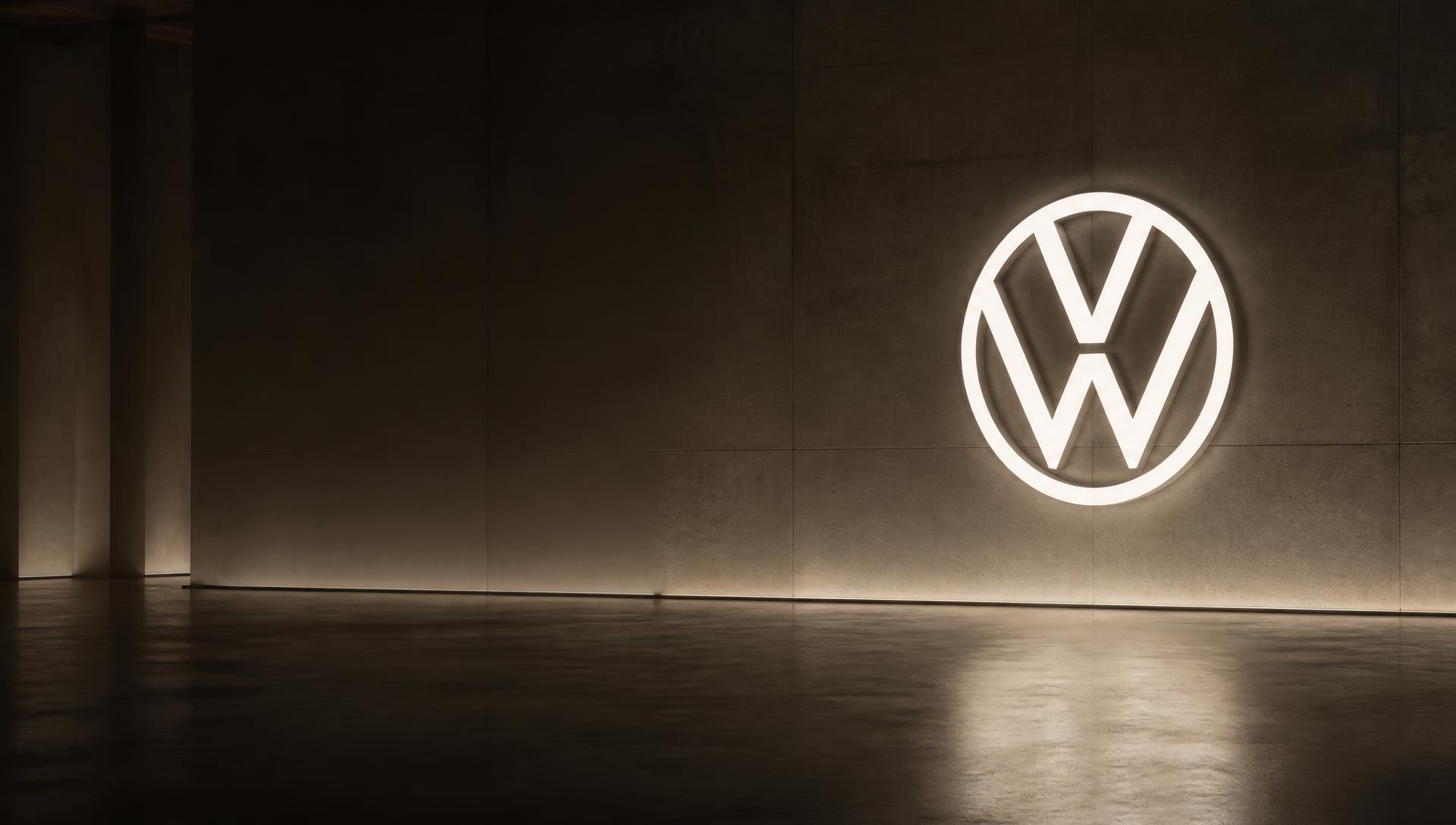 An illuminated Volkswagen emblem on a concrete wall in a quiet, empty showroom